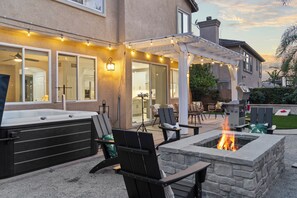 An outdoor patio with a stone fire pit, seating area, and string lights. - Palm Paradise: Hot Tub, Barrel Sauna, Putting, Game Room, Gym (Placentia)
