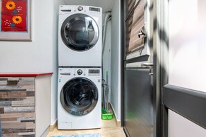 A laundry room with two stacked washing machines, a wooden wall with a red trim, and a green cleaning bucket.