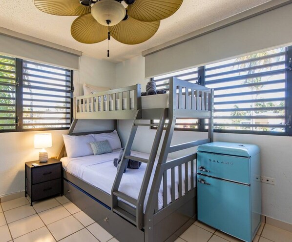 Habitación con literas, un ventilador de techo, una mesita con lámpara y un electrodoméstico azul.