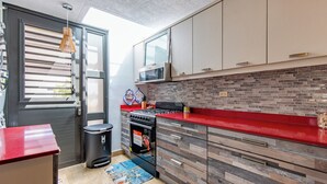 Une cuisine moderne avec un plan de travail rouge, une cuisinière à gaz, un four à micro-ondes et une poubelle.
