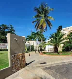 A gated entrance with a stone wall, palm trees, and a clear blue sky.
