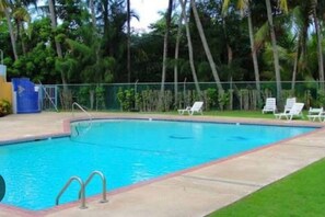 A swimming pool with a surrounding deck, a few lounge chairs, and a fence.