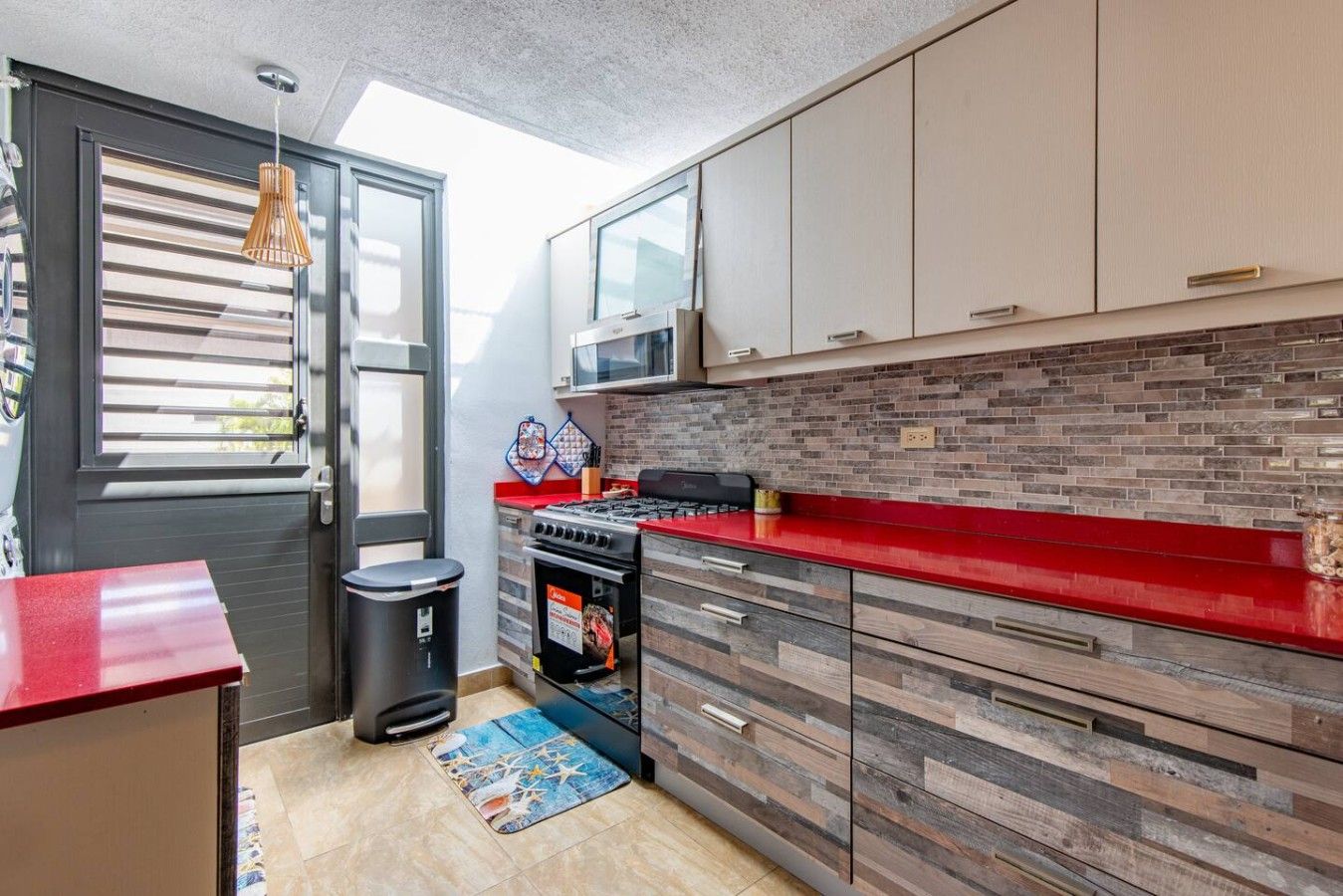 Cozinha compacta com bancada vermelha, fogão a gás, micro-ondas e lixeira.