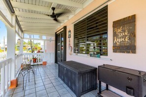 A covered porch with a ceiling fan, a window with blinds, a bench, and a small table.