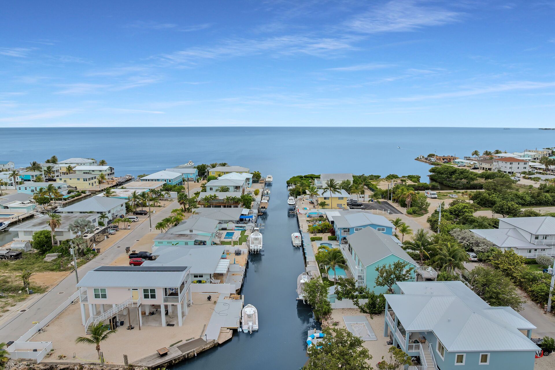 A coastal residential area with houses, a narrow waterway, and a clear view of the ocean.