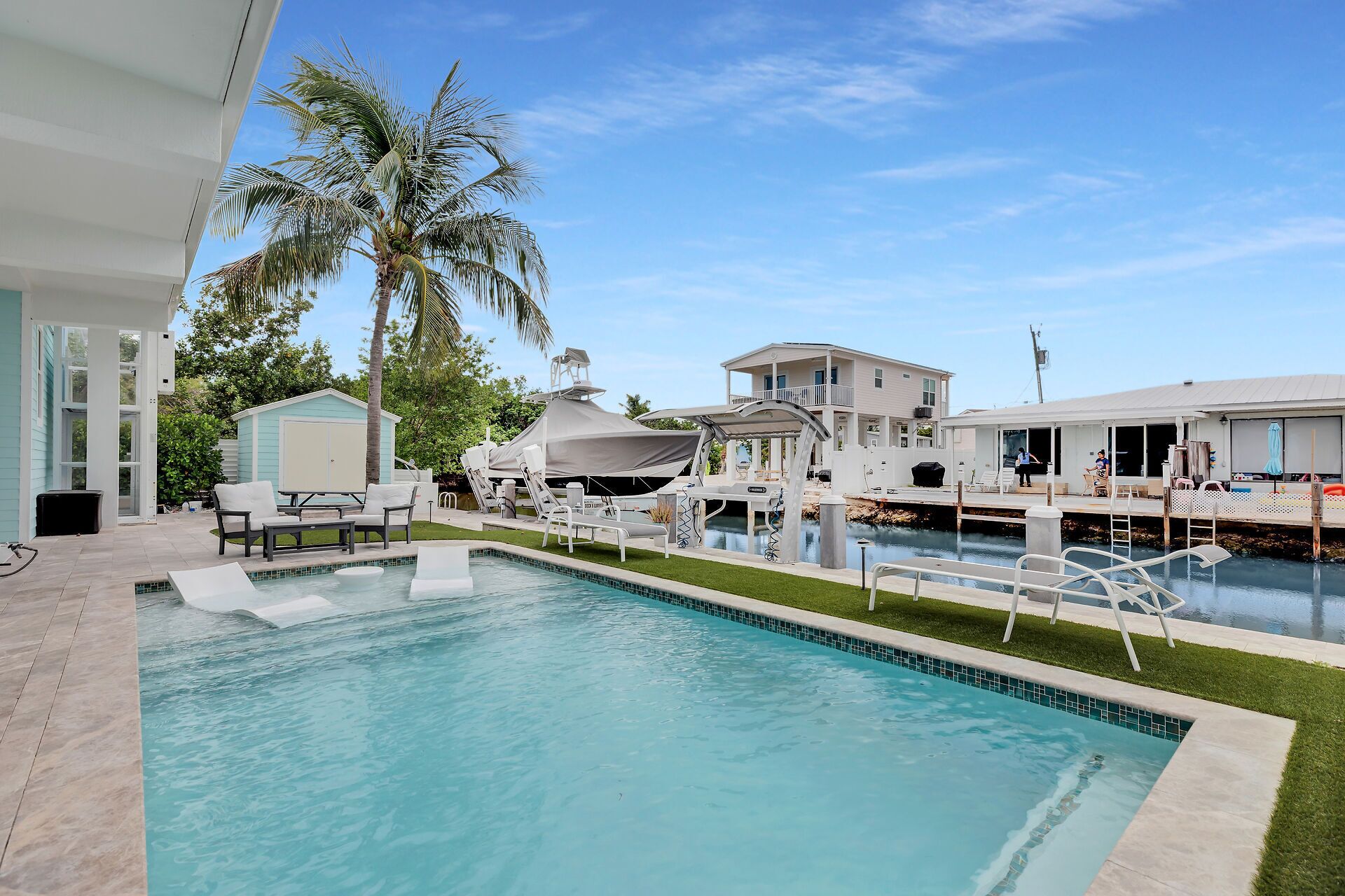 Une piscine avec des chaises longues, un espace abrité et une maison en arrière-plan.