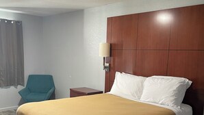 A hotel room with a large bed, a wooden headboard, a bedside lamp, a teal chair, and a wooden floor. - Newly remodeled 14-room hotel in charming St. Mary's . (St. Marys)