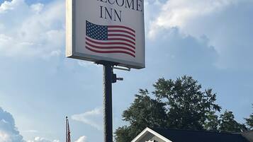 A Welcome Inn sign with an American flag, a Salvation Army building in the background, and a clear sky.