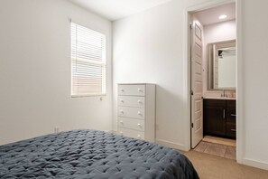 Ein Schlafzimmer mit Bett, Kommode, Schrank und einem Badezimmer mit Spiegel und Waschbecken.