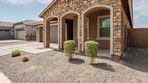 A residential building with a stone facade, multiple garage doors, and a gravel driveway. - Luxurious Arizona Retreat (Queen Creek)