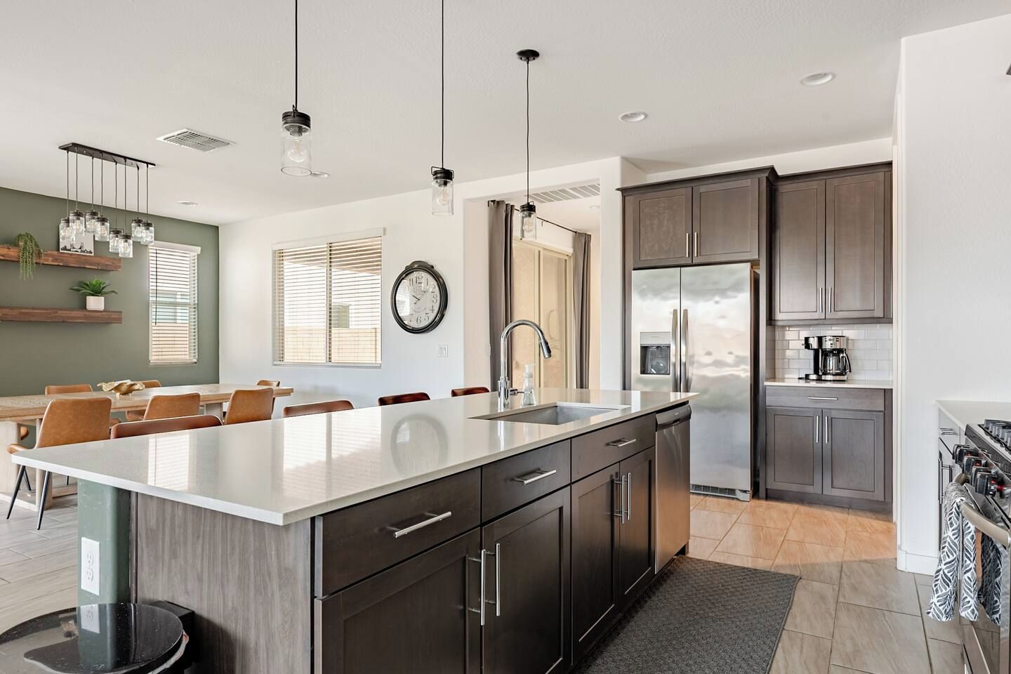A modern kitchen with a large island, dark cabinetry, stainless steel appliances, and pendant lighting.