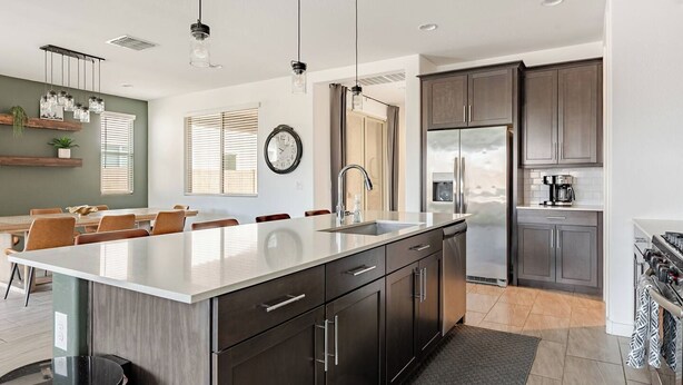 A modern kitchen with a large island, dark cabinetry, stainless steel appliances, and pendant lighting. - Luxurious Arizona Retreat (Queen Creek)