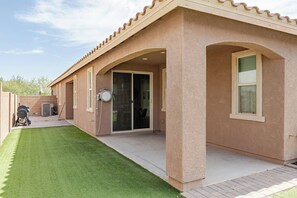 A house with a covered patio, a lawn, and a barbecue grill.