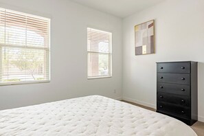 A bedroom with a bed, two windows with blinds, a dresser, and a wall-mounted picture.