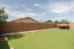 Ein Garten mit Kunstgrasanlage, einer Ziegelmauer und einem überdachten Grillbereich.