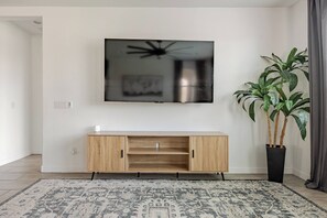 Ein modernes Wohnzimmer mit einem an der Wand befestigten Flachbildfernseher, einer Holzunterhaltungseinheit darunter und einem gemusterten Teppich auf dem Boden.