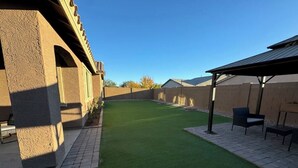 Un jardin avec une pelouse artificielle, une terrasse en briques et un espace salon abrité.
