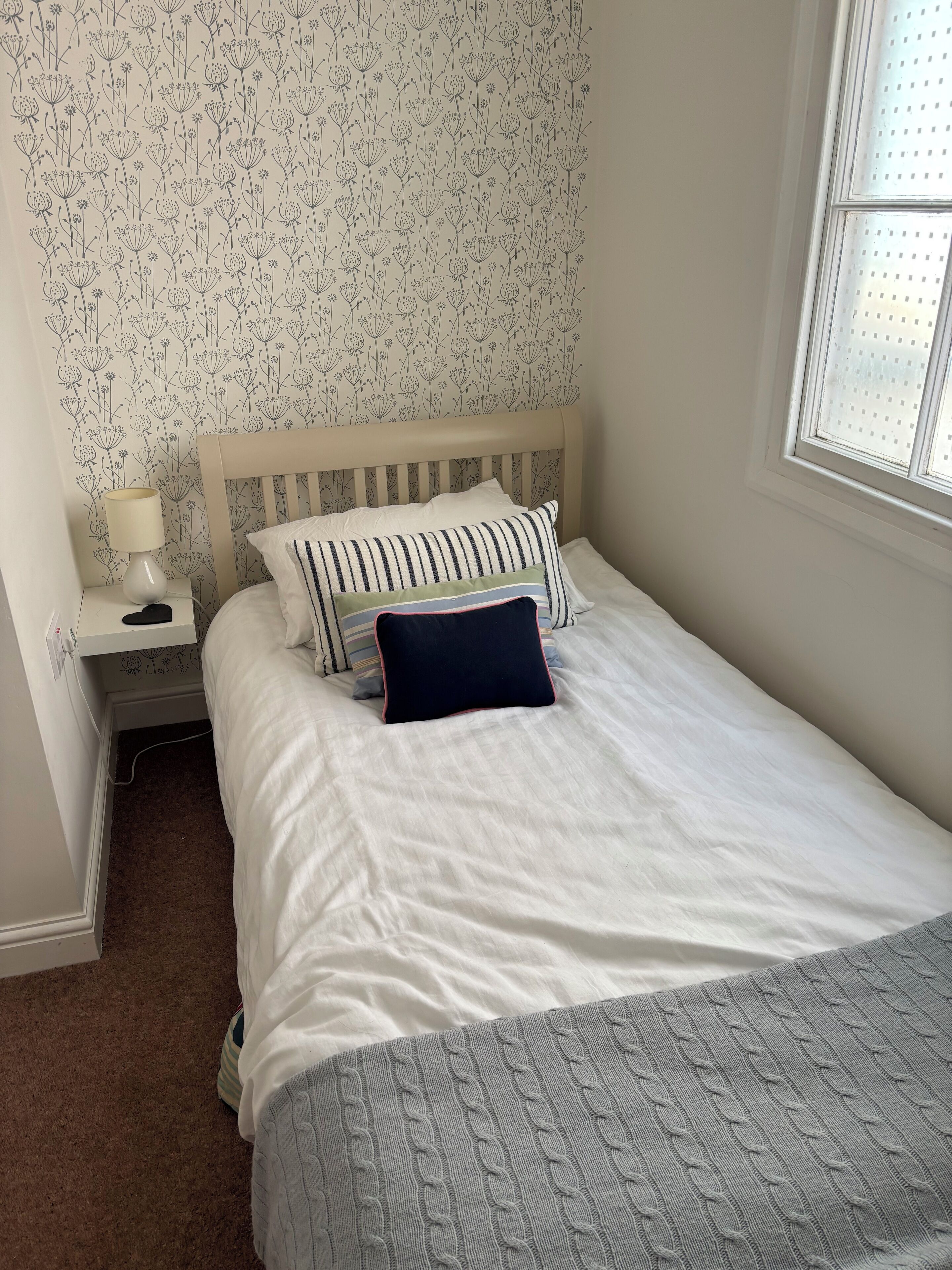 A neatly made bed with white bedding and a grey knitted throw.