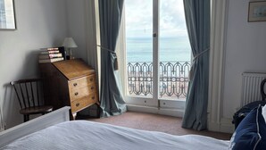 A bedroom with a large bed, a wooden dresser, a chair, and a view of the sea through a balcony. - Hillsborough Terrace (Ilfracombe)