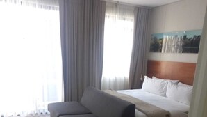 Une chambre d’hôtel avec un lit, un canapé et une grande fenêtre avec des rideaux.