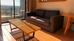 Un salon moderne avec un canapé, une table en bois et une vue sur le paysage urbain, visible à travers de grandes fenêtres.