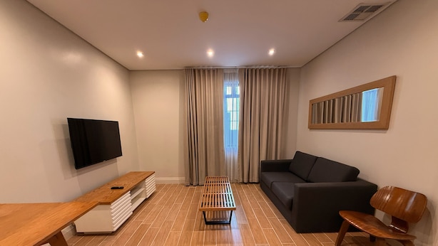 Un salon moderne avec une table basse en bois, un canapé noir, un banc en bois et un téléviseur fixé au mur.