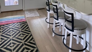 A kitchen with white cabinets, a large window, and a bar stool area.