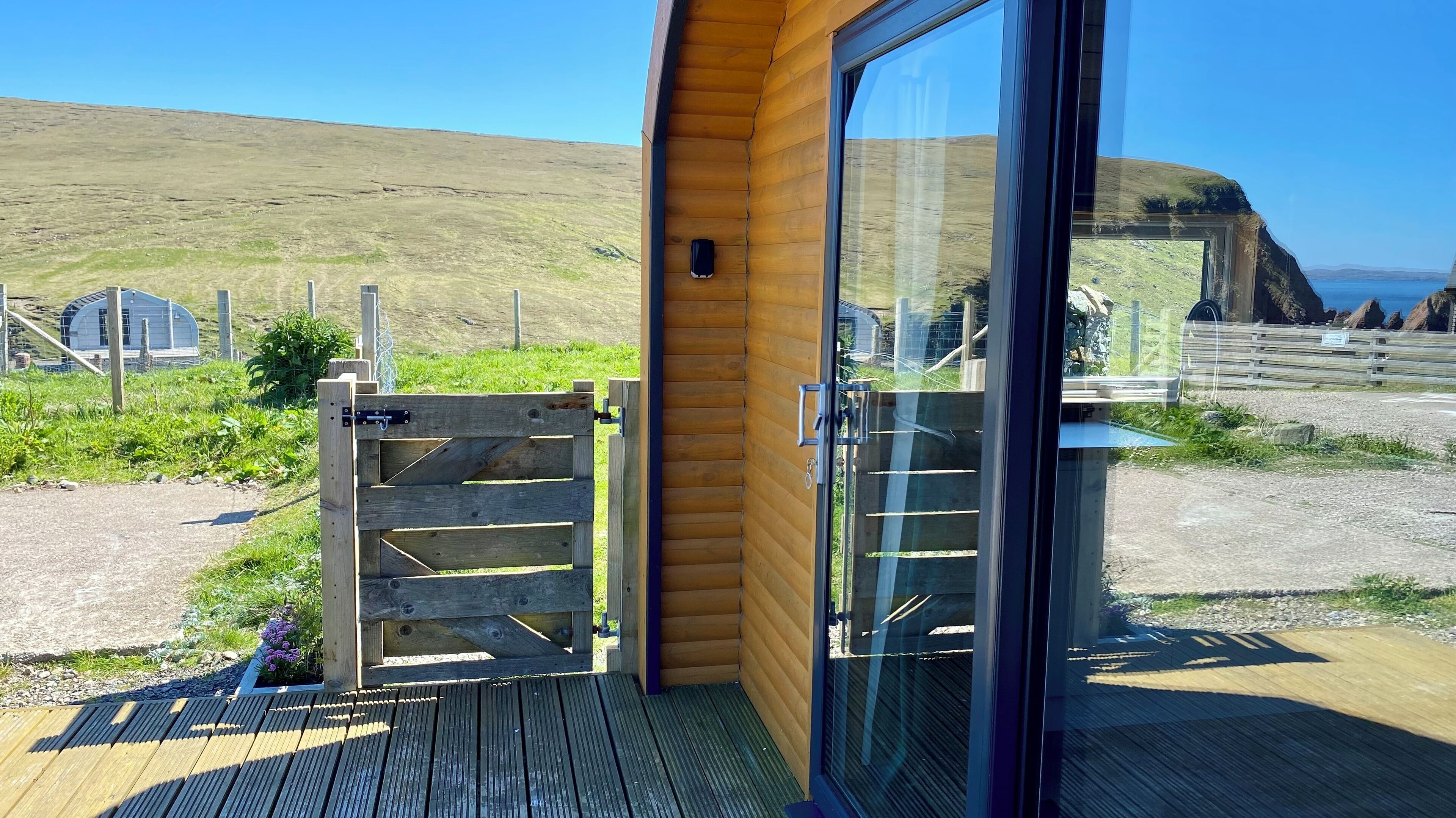 A wooden cabin with a glass door, a wooden deck, and a view of a coastal landscape.