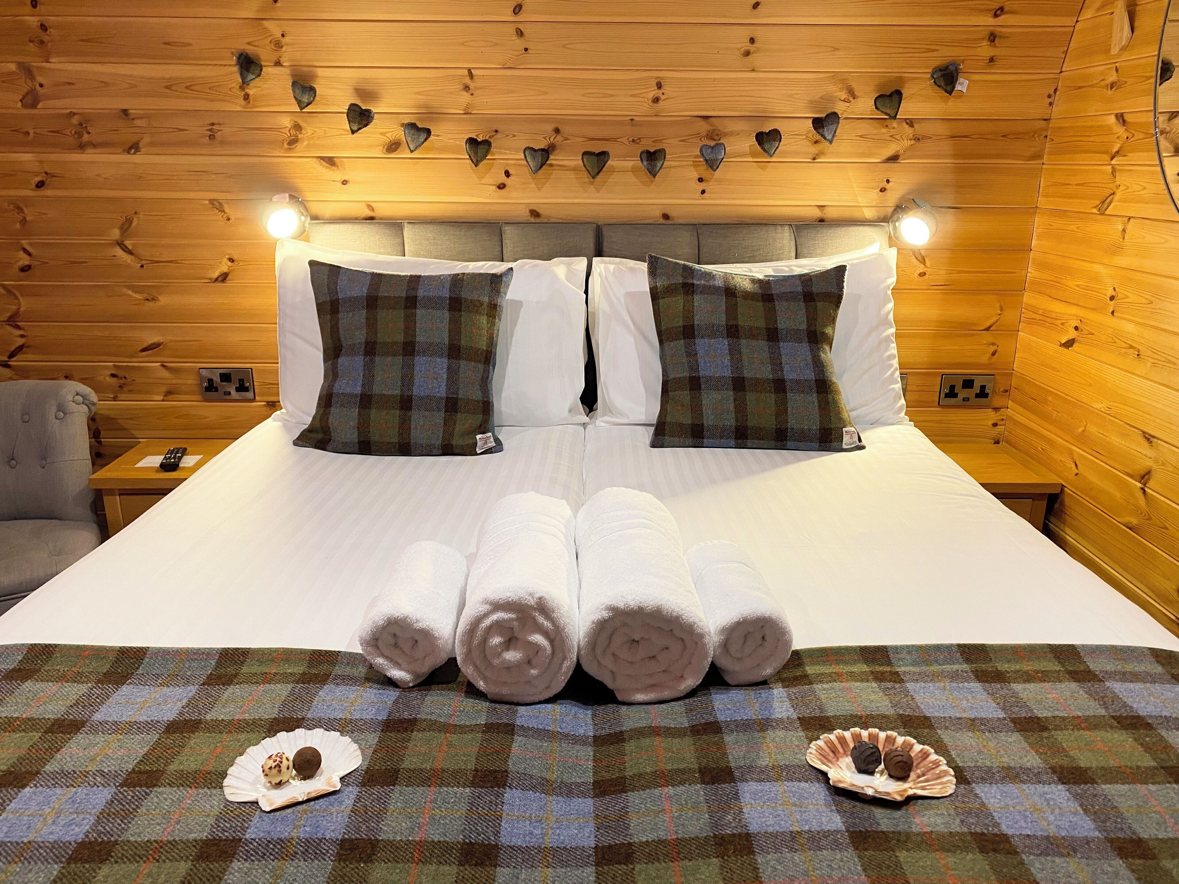 A wooden cabin room with a bed, two nightstands, and heart-shaped wall decorations.