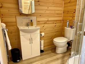 A wooden-paneled bathroom with a sink, toilet, and a glass shower enclosure.
