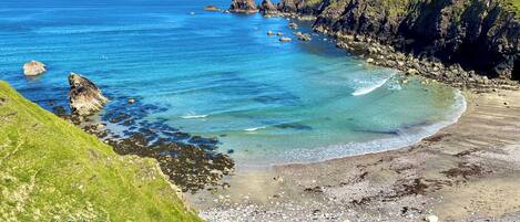 A coastal landscape with clear blue waters, rocky shorelines, and grassy hills.