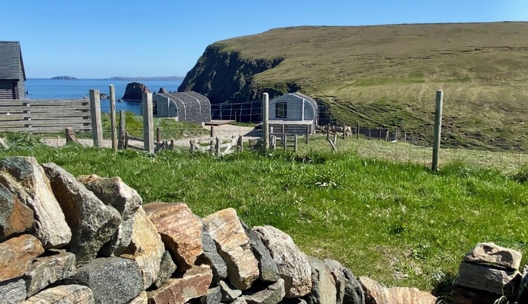 A coastal property with stone walls, a wooden fence, and a grassy area.