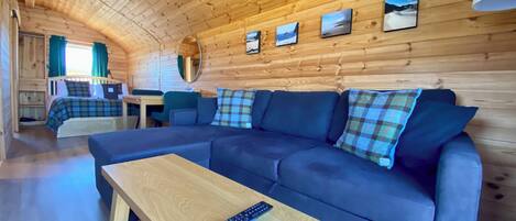 L’intérieur d’un chalet accueillant, avec un canapé, une table, un miroir et un lit.