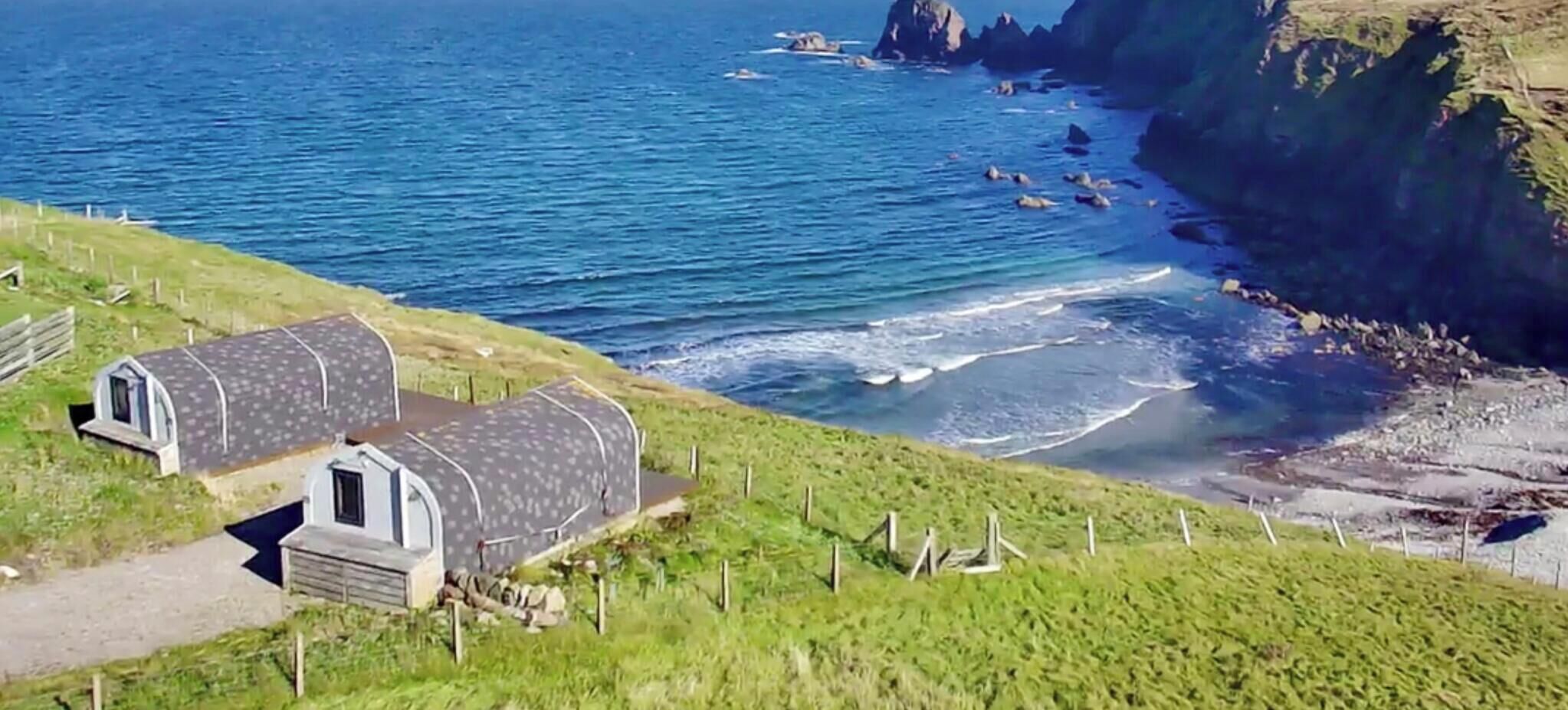Una proprietà costiera con due piccole strutture a cupola, una zona verde e un litorale roccioso.