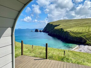 A coastal view from a covered deck with a wooden floor, grassy terrain, and a clear blue sea. - SEApods Luxury Glamping - Isle of Lewis (Isle of Lewis)