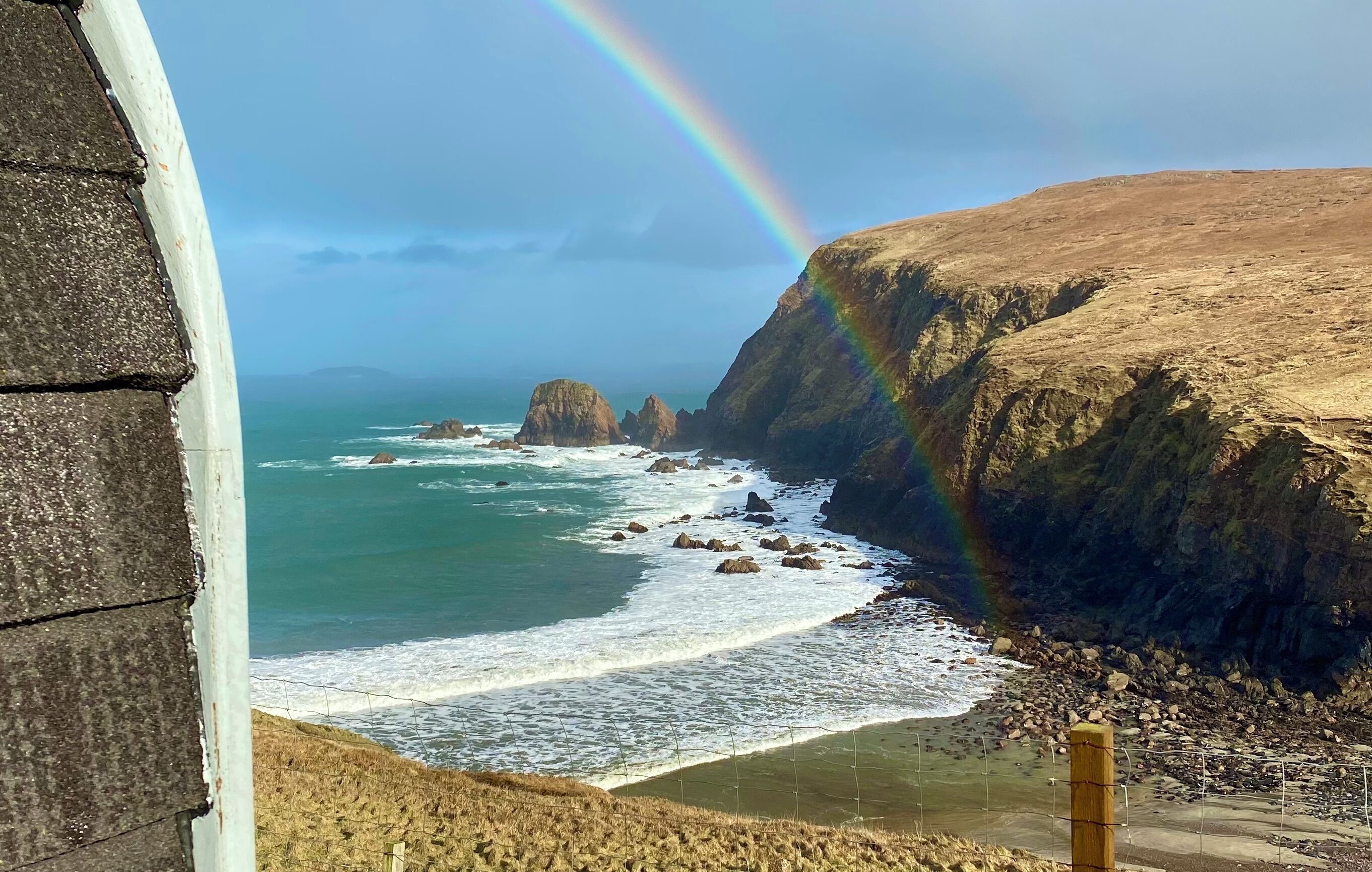 A coastal landscape with a rainbow, rocky cliffs, and the ocean.