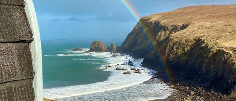A coastal landscape with a rainbow, rocky cliffs, and the ocean.