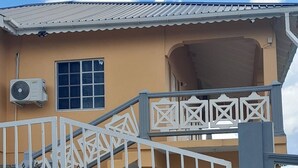 Un edificio con facciata beige, un cancello bianco con decorazioni e una scala che conduce a un balcone.