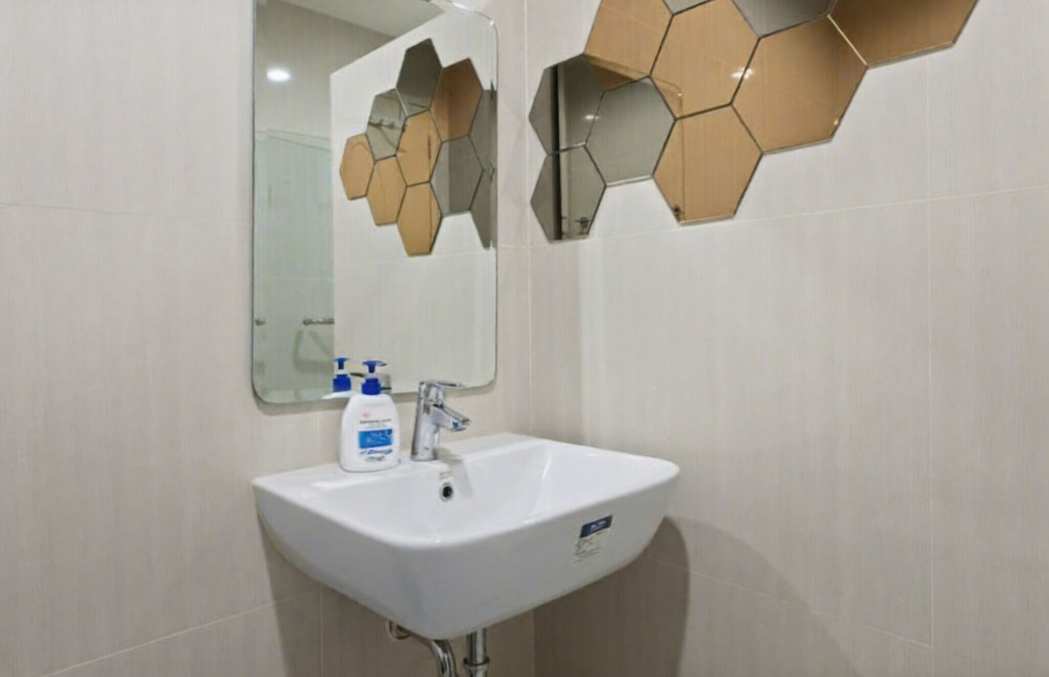 Casa de banho com lavatório branco, espelho e azulejos hexagonais na parede.
