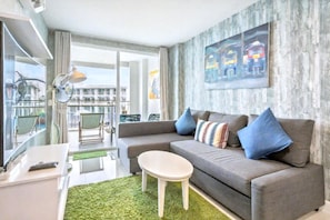A modern living room with a grey sofa, a small white coffee table, and a green rug. There is a large window with a view of buildings and a balcony. - The Energy Hua Hin - 1 Bedroom Condo With Seaview (Cha-am)