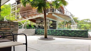 A modern building with a spiral staircase, a palm tree, and a stone wall. - Emerald 215 - Studio With Balcony and Shared Pool (Patong)