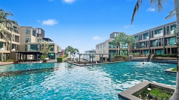A swimming pool surrounded by modern buildings with large windows and balconies, and a clear blue sky. - Pixel-modern 1-br Apartment With Pool View in Cape Panwa (Wichit)