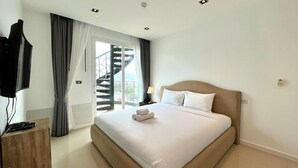 A hotel room with a large bed, a TV, a desk with a keyboard, and a window with curtains.