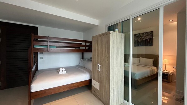 Une chambre avec un lit superposé, une armoire, une porte vitrée donnant sur une autre pièce et un lit avec une lampe.