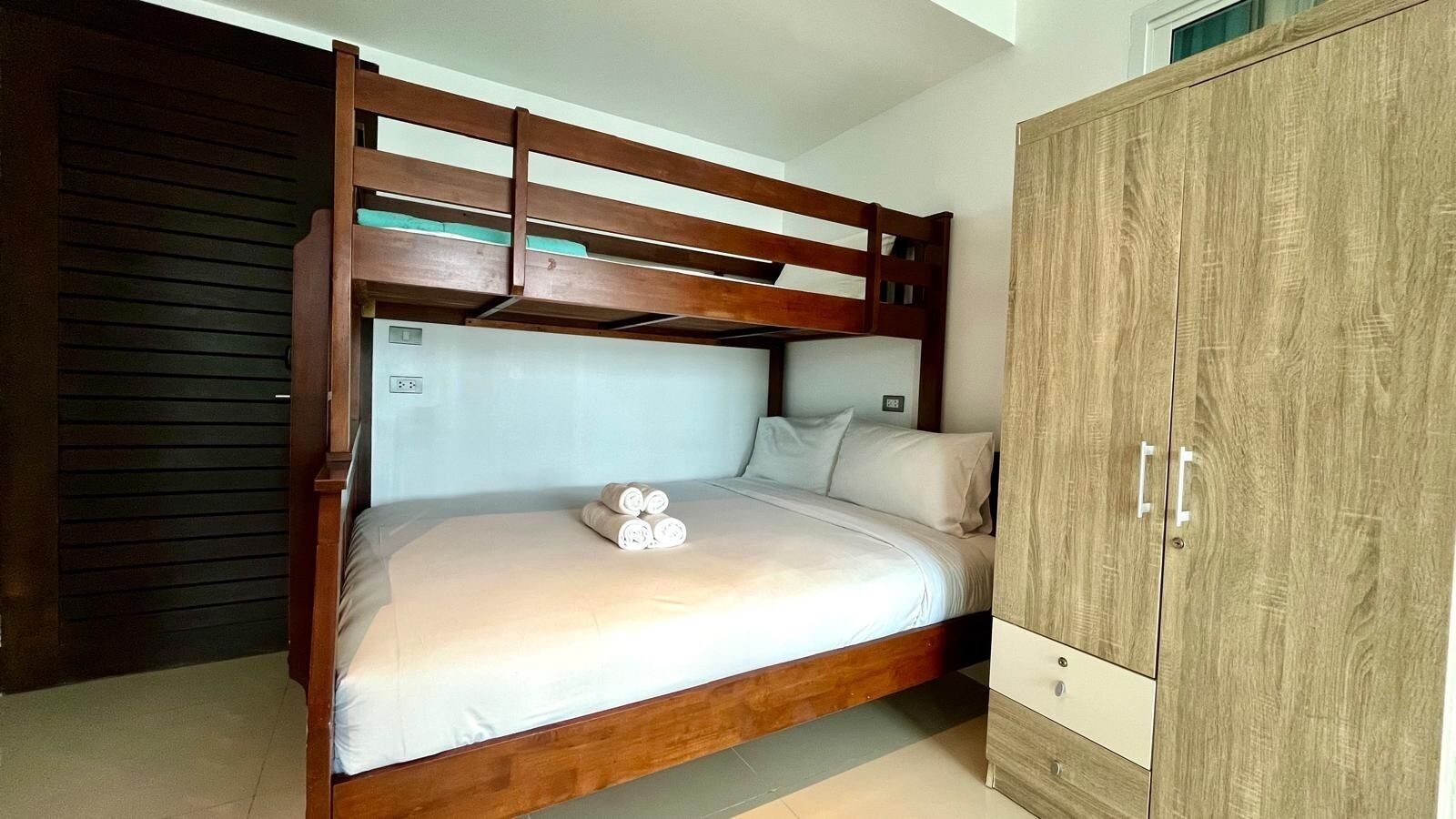 A bunk bed with a wooden frame and a single bed below. There is a wooden wardrobe to the right.