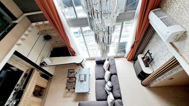 Ein modernes Wohnzimmer mit einer Couch, einem Couchtisch und einem Fernseher. Ein Fenster mit Vorhängen und einer Hängelampe sind zu sehen.