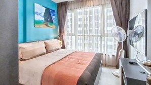 Ein Schlafzimmer mit einem Bett, einem Fernseher, einem Schreibtisch und einem Fenster mit Vorhängen.