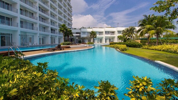 A swimming pool surrounded by lush greenery and a multi-story hotel building. - 1703 - 2 Bdr Condo Seaview Boathouse Hua Hin (Cha-am)