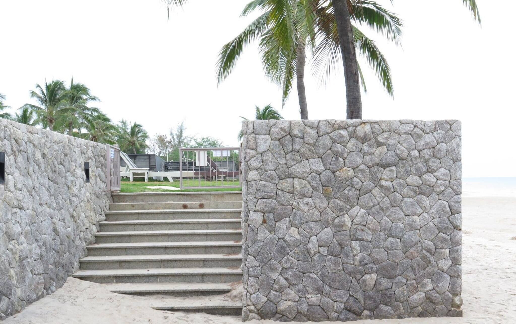 A stone staircase leading to a beach area with palm trees and a view of the ocean.
