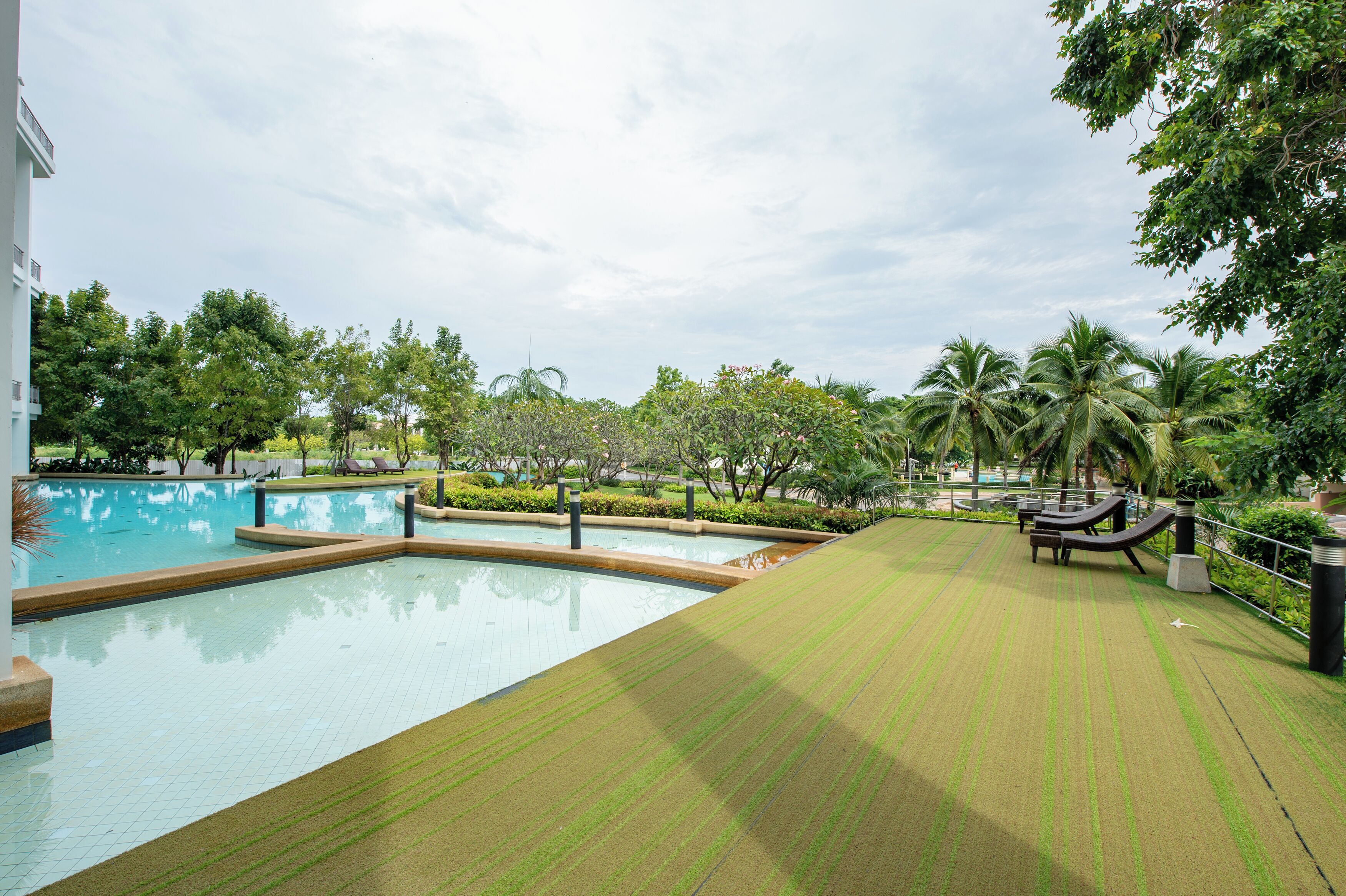 A swimming pool with a tiled deck, surrounded by palm trees and greenery.